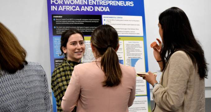 one student smiling in front of a poster talking to two other students